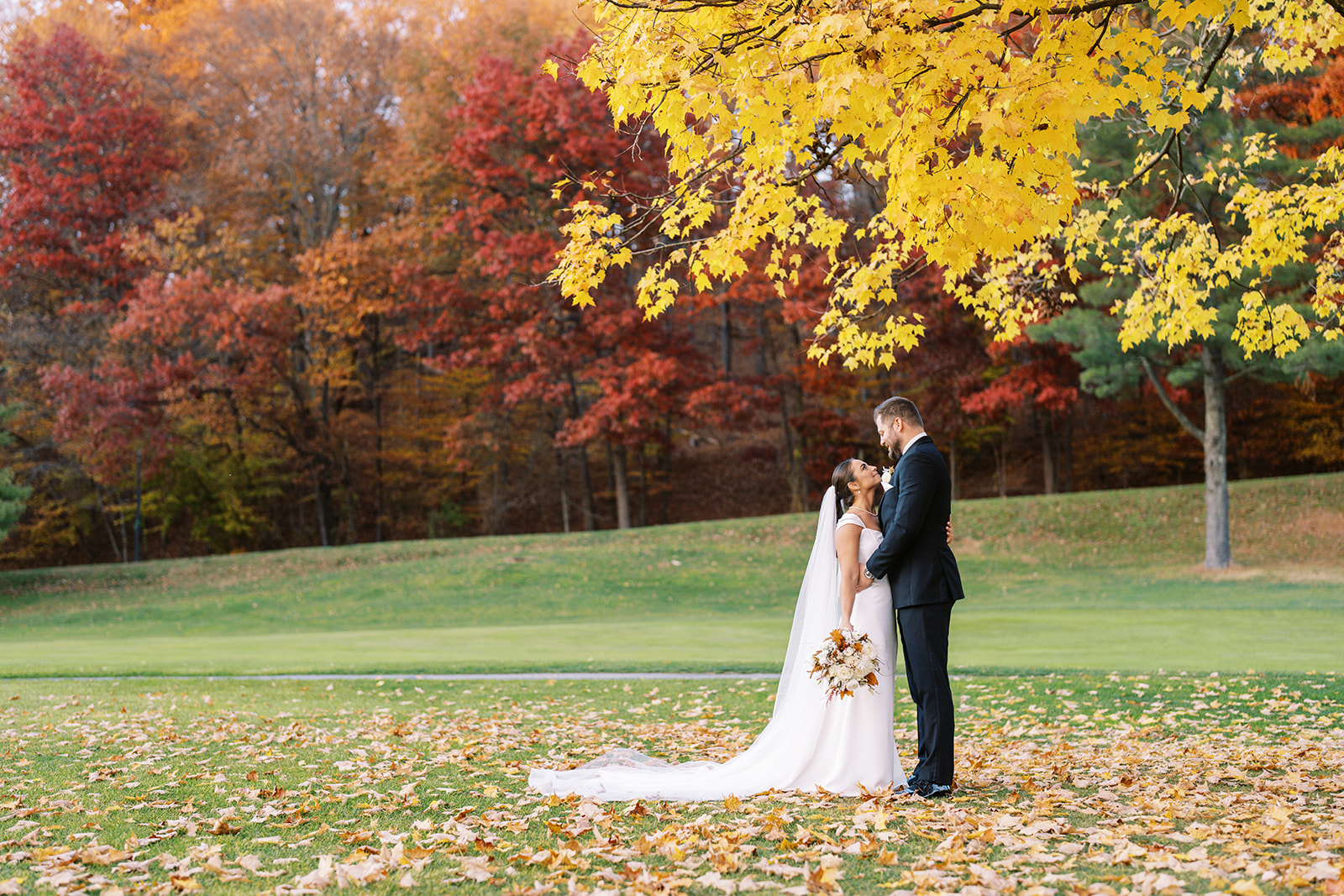 A couple, just married, embraces under vibrant autumn leaves.